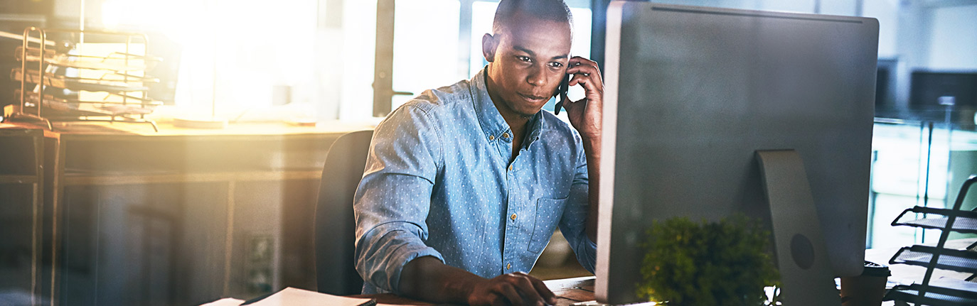 Person on phone in front of their computer checking their estatments.