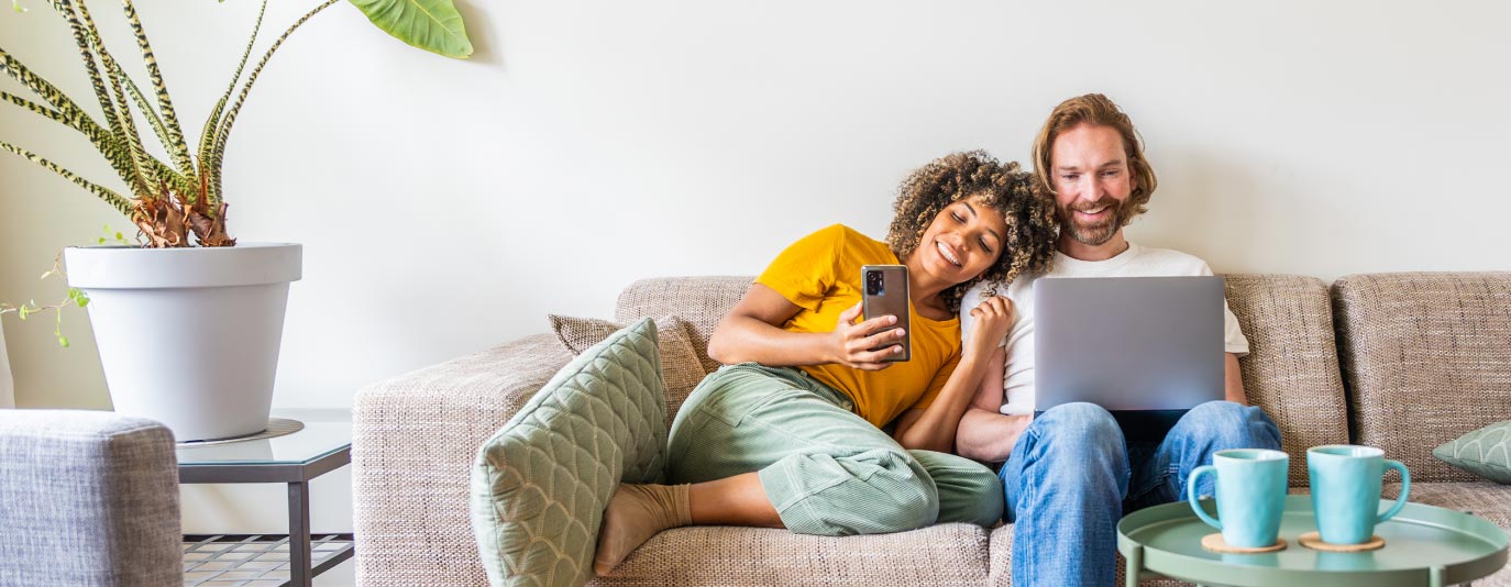 A young couple using laptop and smart phone sitting on the sofa at home